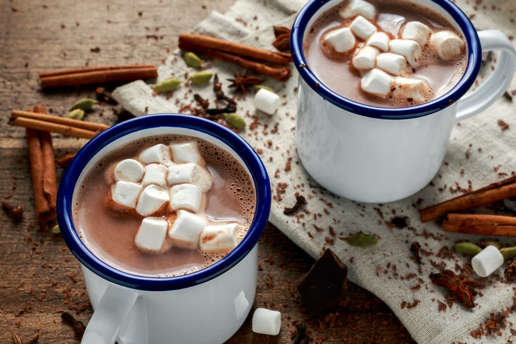 Two mugs of hot cocoa with marshmallows on a wooden background with cinnamon